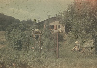 Vintage sepia-toned photo of a rural homestead with a two-story wooden house and elevated wooden platform. Early 20th-century...