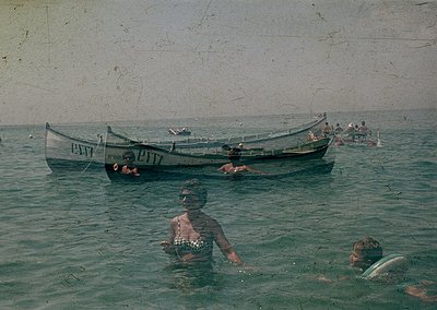 Vintage seaside scene featuring two wooden boats labeled "ПИТТ" in Cyrillic, likely Bulgarian. A woman in a patterned swimsui...