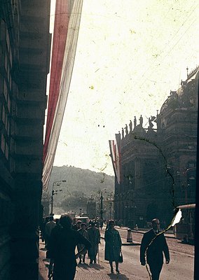 Vintage sepia-toned street scene featuring early 20th-century European architecture with ornate facades and wrought-iron balc...