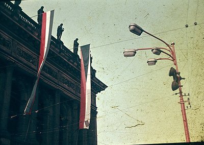 Vintage sepia-toned photo of a grand, ornate building facade with intricate carvings and two red-and-white striped banners. T...