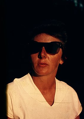 Portrait of an individual in vintage sunglasses, likely from the 1960s–1970s. Light-colored, loose-fitting blouse with a V-ne...