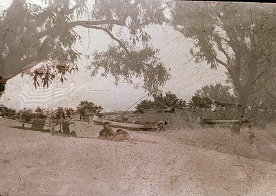 Vintage sepia-toned photo of a rural scene with a horse-drawn cart on a dirt road, flanked by sparse trees and shrubs. The im...