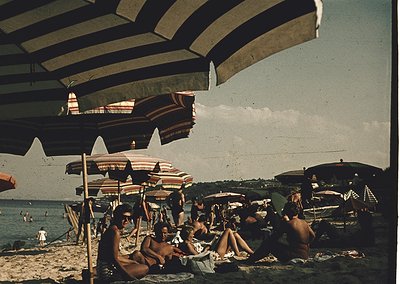 Vintage seaside scene with striped beach umbrellas and mid-century swimwear. Crowded sandy shore with people lounging, wading...