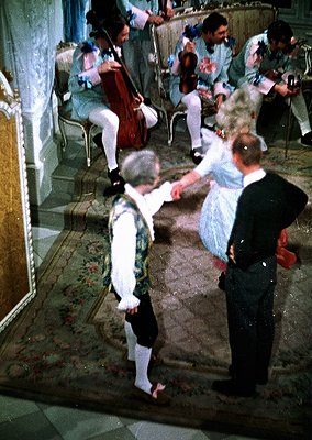 Vintage ballroom scene featuring classical attire: a man in 18th-century formal wear (white breeches, vest, stockings) dancin...