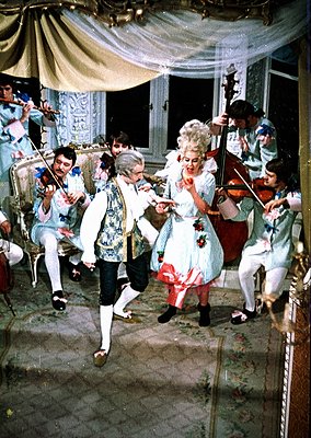 19th-century costume ballroom scene with string quartet performing. Men in tailored white coats with cravats, women in elabor...