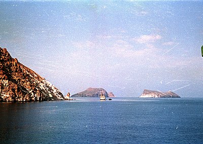 Vintage coastal scene featuring jagged limestone cliffs and two small rocky islets in calm waters. Soft vintage filter sugges...