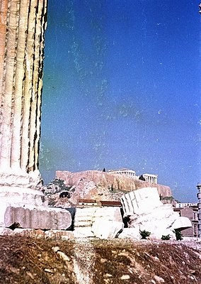 Ancient Greek ruins framed by a weathered column, likely the Parthenon’s Acropolis, Athens, Greece. Marble fragments and clas...