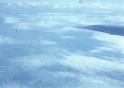 Vintage aerial view of a snow-covered landscape with subtle, wavy terrain patterns. Likely captured during winter, possibly m...