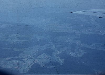 Aerial view of a coastal salt evaporation pond system, likely for industrial salt harvesting. The geometric, shallow pools cr...