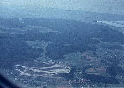 Aerial view of rural terrain with winding roads and agricultural fields, likely mid-20th century. Dense forest patches contra...