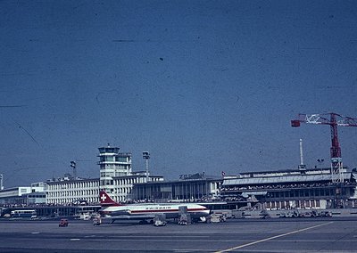 Mid-20th century airport terminal with Swissair jet in foreground. Brutalist architecture with concrete towers and geometric ...