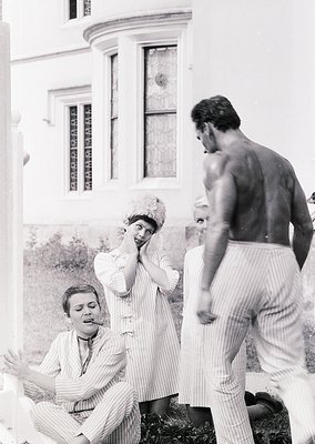 Vintage black-and-white photo of three individuals in 1960s beachwear—striped swim trunks and a woman in a striped dress with...