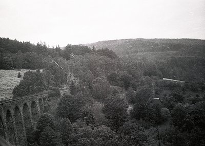 Black-and-white aerial view of a **viaduct bridge** spanning a forested valley, likely mid-20th century. The **multi-arched s...