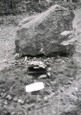 Blurred vintage monochrome shot of a large, irregularly shaped boulder on a gravel path, surrounded by scattered stones and f...