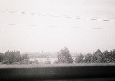 Vintage black-and-white landscape featuring misty horizon with dense tree line and distant church spire. Overcast sky and pow...