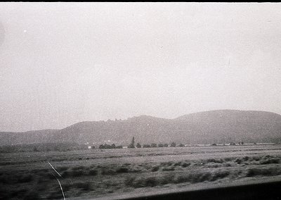 Vintage black-and-white landscape showing rolling hills and sparse vegetation, likely mid-20th century. Flat terrain dominate...