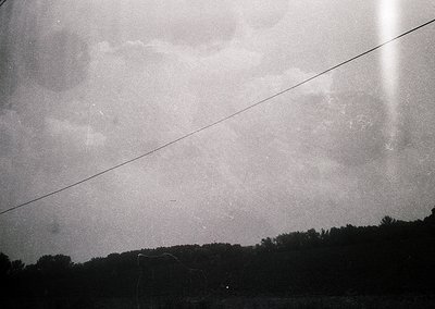 Black-and-white shot of a low-angle sky framed by power lines, evoking mid-20th century documentary style. Dense, overcast cl...