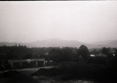 Vintage black-and-white view of a rural landscape featuring a low-lying industrial building complex with flat roofs and minim...