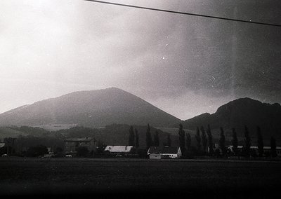Vintage black-and-white rural landscape featuring rolling hills and scattered farmhouses. Low-angle shot captures misty horiz...