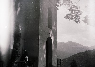 Vintage black-and-white photo of a lone figure ascending a stone staircase toward a bell tower entrance, framed by architectu...