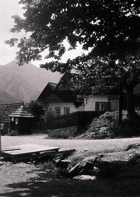 Rustic alpine cottage with wooden exterior and pitched roof nestled in a forested valley. Stone pathway and wooden bench in f...