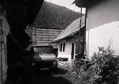 Classic mid-century Alpine cottage with rustic stonework and wooden shingle roof, nestled in a forested valley. A vintage van...