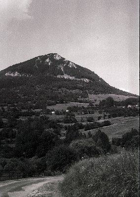 Black-and-white landscape featuring a steep, rocky hillside dominating the background, likely part of a mountainous region. S...