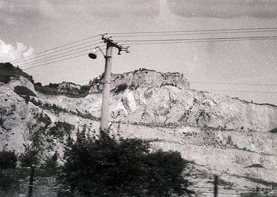 Mid-20th century black-and-white photo of rugged mountainous terrain with utility pole and power lines. Barren hillsides sugg...