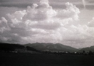 Black-and-white aerial view of rolling hills and scattered buildings, framed by horizontal window bars. Likely mid-20th centu...