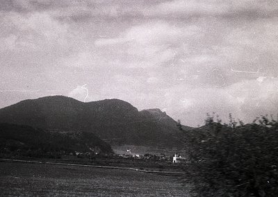 Vintage black-and-white landscape featuring rolling hills and a distant village under stormy skies. Low-angle shot captures m...