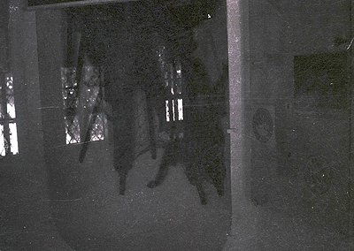 Vintage grayscale shadow projection on a textured wall, likely from a slide projector. Silhouettes of two figures in mid-stri...