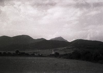 Black-and-white landscape featuring rolling hills and a lone utility pole with power lines stretching diagonally across the f...