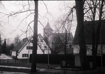 Black-and-white shot of a **half-timbered Tudor-style church** with a steep gable roof and central tower, framed by bare wint...