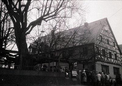 Timber-framed half-timbered building with exposed beams, likely a traditional European inn or restaurant. Crowd of people gat...