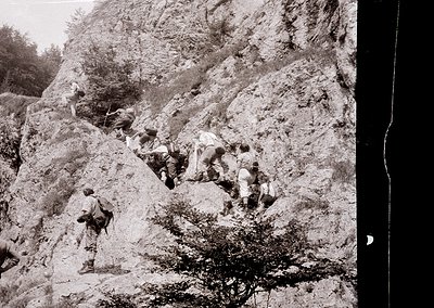 Black-and-white photo of a group of soldiers ascending a rugged, rocky mountain trail, likely during WWI or WWII. Uniforms su...