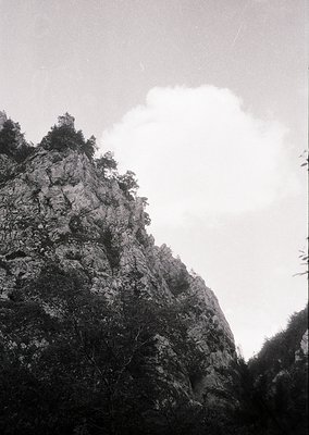 Monochrome mountain peak with rugged, vertical rock face and sparse vegetation. Dramatic cloud formation partially obscures s...