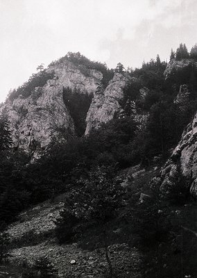 Monochrome mountain landscape with steep rocky slopes and sparse vegetation. Dramatic vertical rock formations dominate the s...