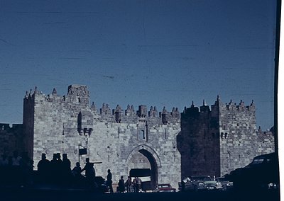 Historic stone gate with crenellated towers, likely the Jaffa Gate in Jerusalem’s Old City. Mid-20th century architecture wit...