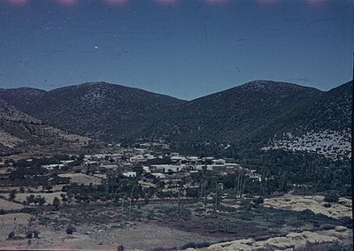 Vintage sepia-toned aerial view of a rural settlement nestled between barren hills, likely mid-20th century. Clustered low-ri...