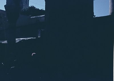 High-contrast monochrome shot of a shadowy interior space, likely a balcony or covered terrace. Partial view of a wooden rail...
