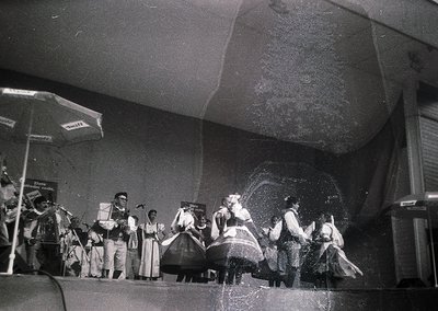 Black-and-white stage performance featuring traditional folk dancers in elaborate costumes, likely Eastern European. Musician...