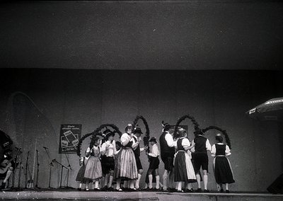 Black-and-white stage performance featuring traditional Alpine folk attire—women in full skirts, blouses, and headscarves, me...