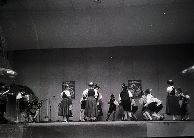 Mid-20th century stage performance featuring traditional folk dancers in regional attire, likely Eastern European. Group incl...