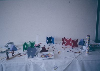 Handcrafted paper butterflies, elephants, and geometric shapes decorate a tabletop with confetti and a lace tablecloth. Mid-2...