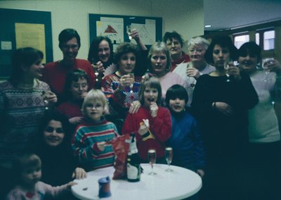 Vintage group photo from the 1980s featuring adults and children in festive attire, likely a holiday gathering. Indoor settin...
