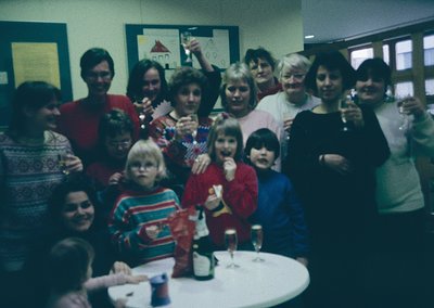 Vintage group photo from the 1970s–80s, likely a community or family gathering. Indoor setting with casual attire—striped swe...