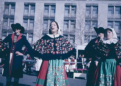 Traditional folk dancers in elaborate embroidered costumes, featuring floral patterns and layered skirts, perform outdoors. T...