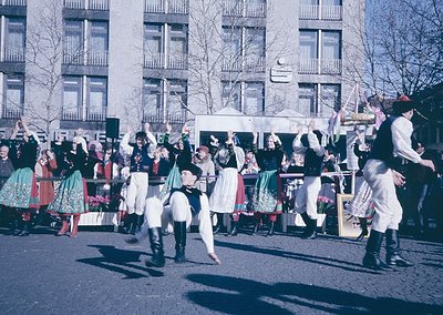 Vibrant street parade featuring traditional folk dancers in colorful, embroidered costumes—men in vests, hats, and knee-high ...