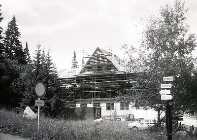 Mid-20th century alpine building under scaffolding, likely a chalet or resort. Distinctive gabled roof and wooden framing vis...
