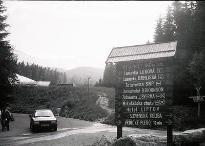 Black-and-white alpine road signpost listing destinations: Lanovka Lukova, Lanovka Brhliska, Zotavna J. Šverma, Mikuláška cha...